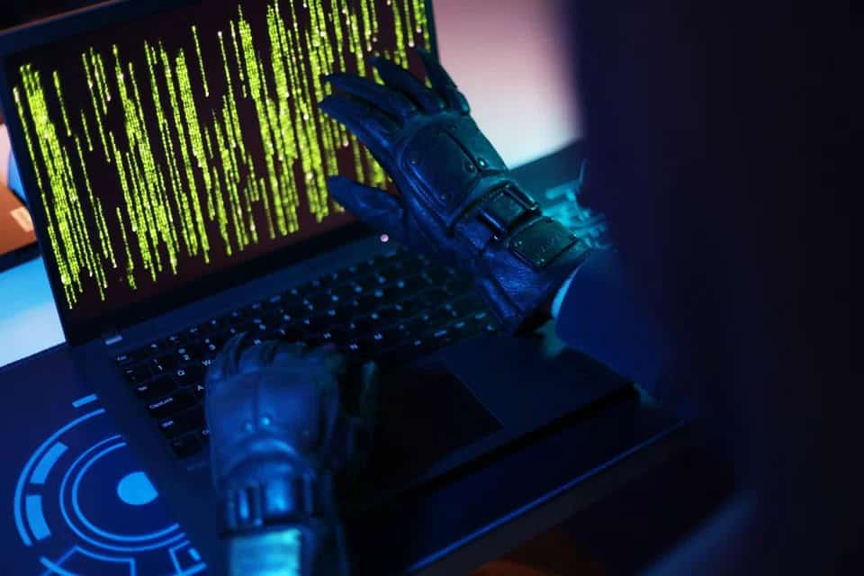 Hacker in gloves accessing a computer with green code on screen.